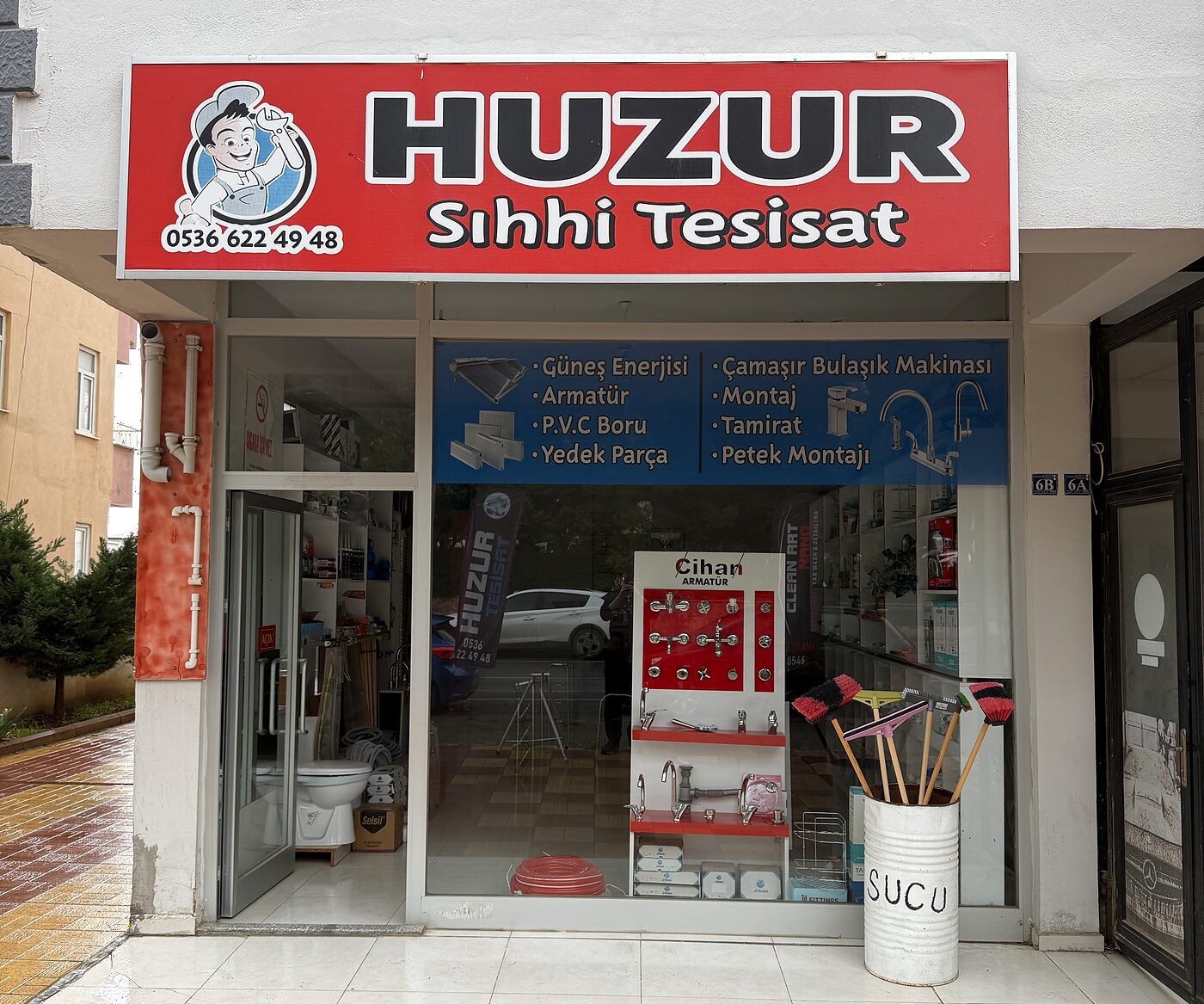 Huzur Sıhhi Tesisat dükkanının önü: kırmızı tabela ve tesisat malzemeleriyle dolu vitrin